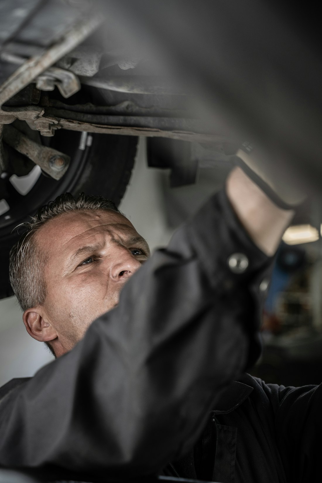 Mekaniker, der arbejder omhyggeligt under en løftet bil